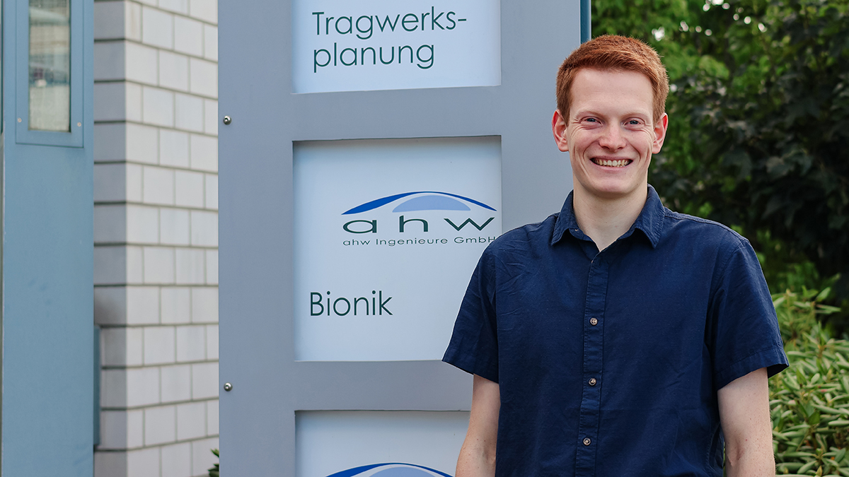 Felix Röhlke steht vor einem Schild mit dem ahw Logo. Im Hintergrund sind das ahw Bürogebäude und grüne Büsche.