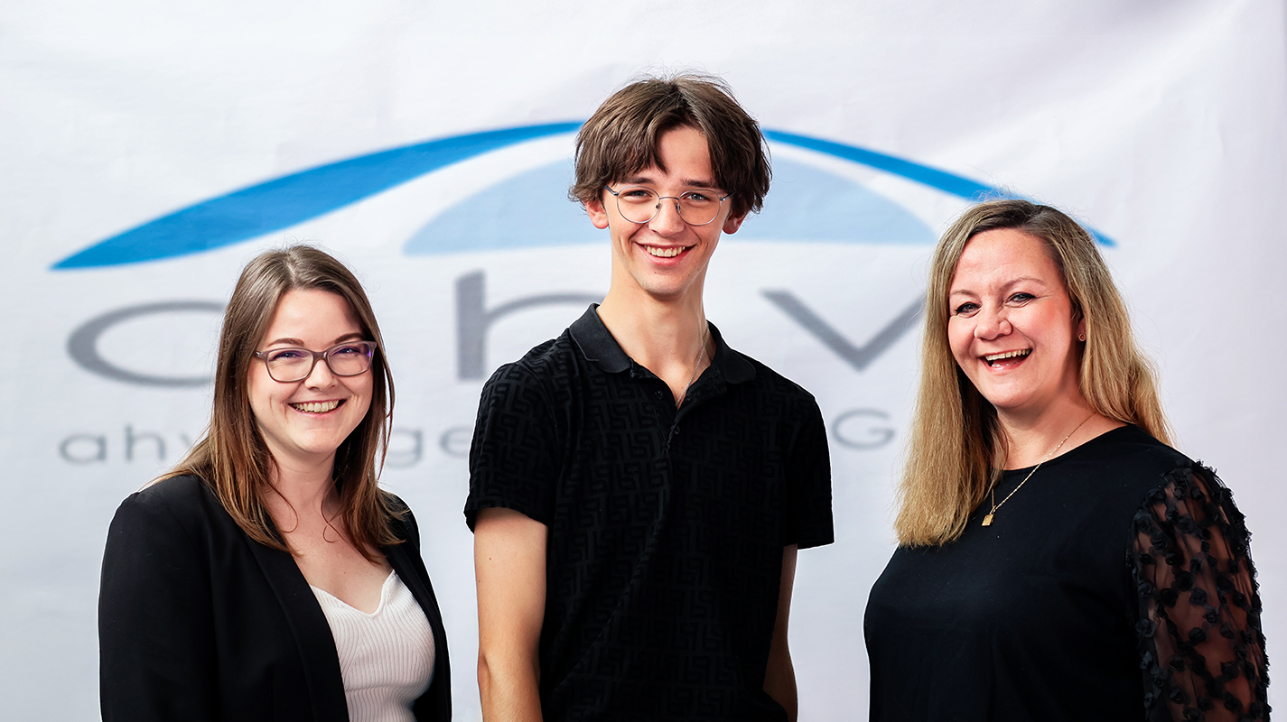 Ellen Holtmannspötter (links), Colin Fehmer (mitte) der neue Azubi, und Christina Beermann (rechts). Im Hintergrund ist das ahw Logo groß zu sehen.