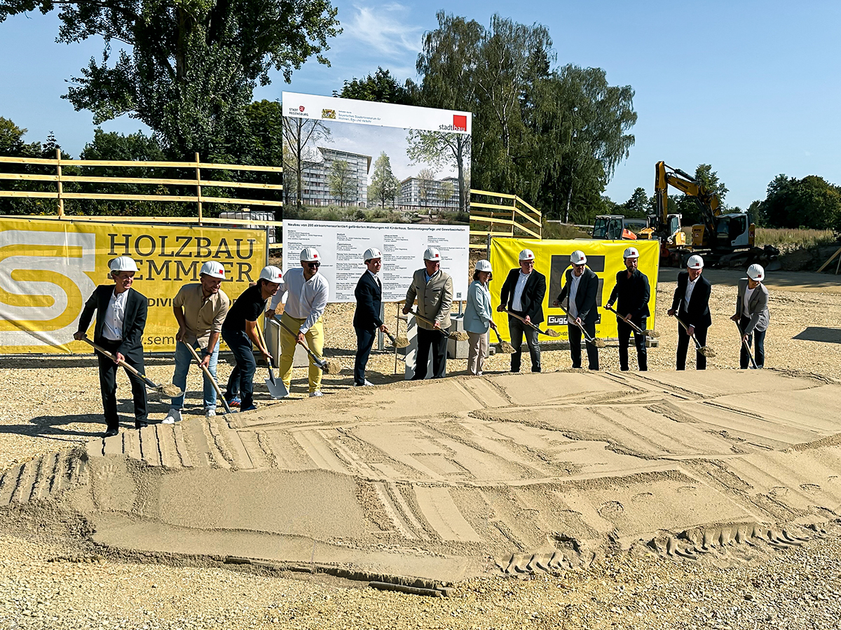 Spatenstich auf dem PLK-Areal: Mehrere Beteiligte stehen mit Spaten im Sand vor einer Projektvisualisierung des zukünftigen Wohnquartiers.